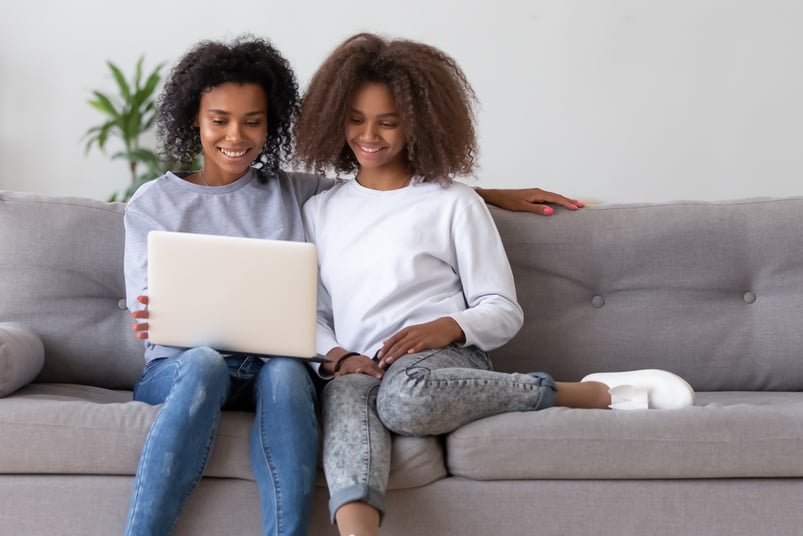 Happy african mother and teen daughter using laptop on sofa